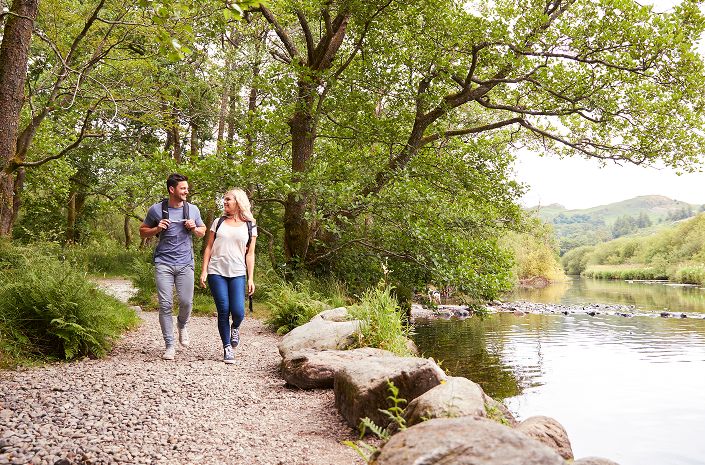 A man and woman walk together along a river path, experiencing the tranquility of The Parkstone Amenities.