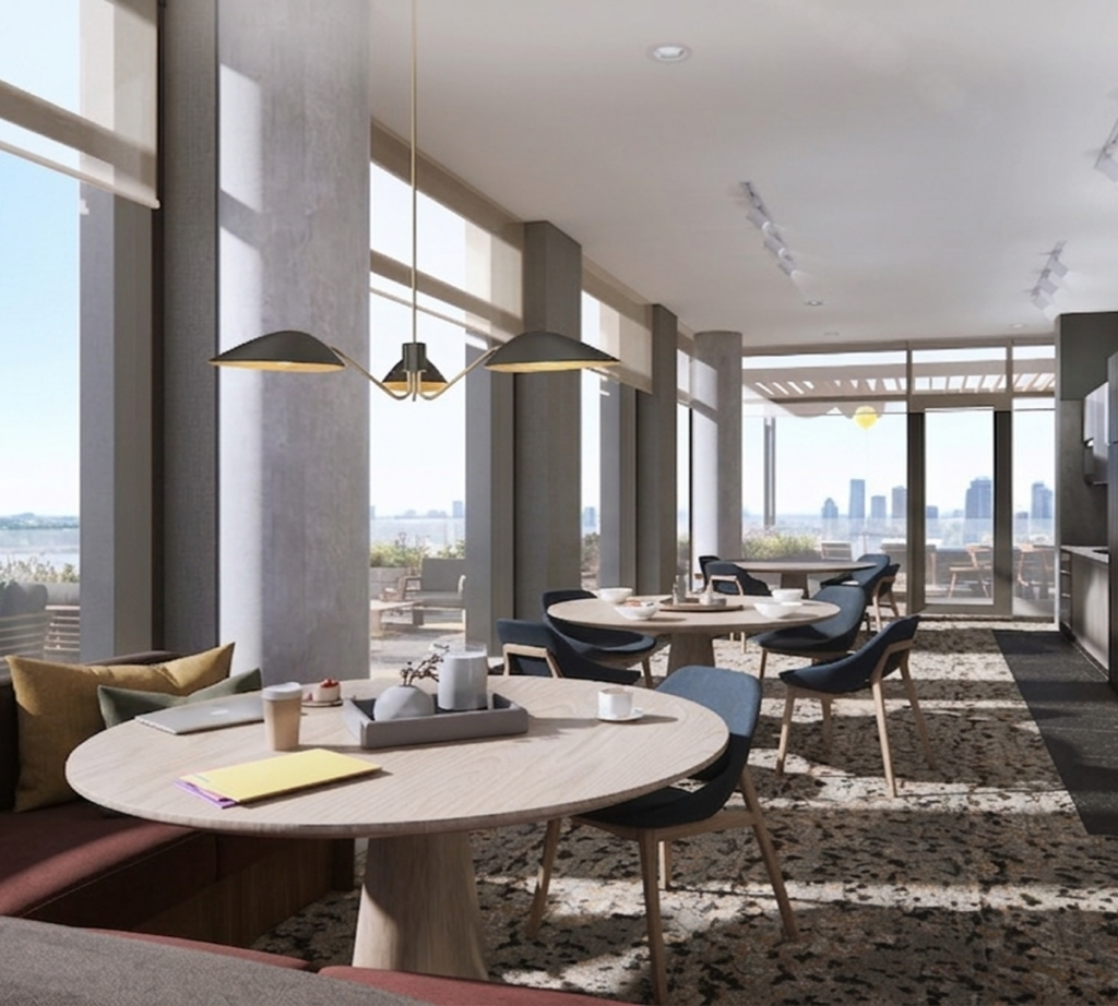 Bright apartment lounge with round tables, large windows, and a city view.